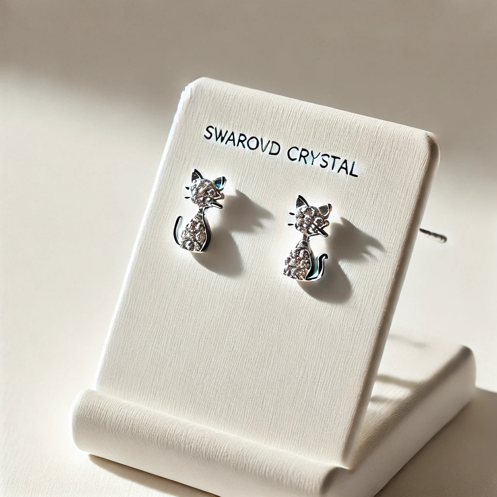 Petites boucles d’oreilles en cristaux Swarovski avec design félin minimaliste, exposées sur un support blanc moderne